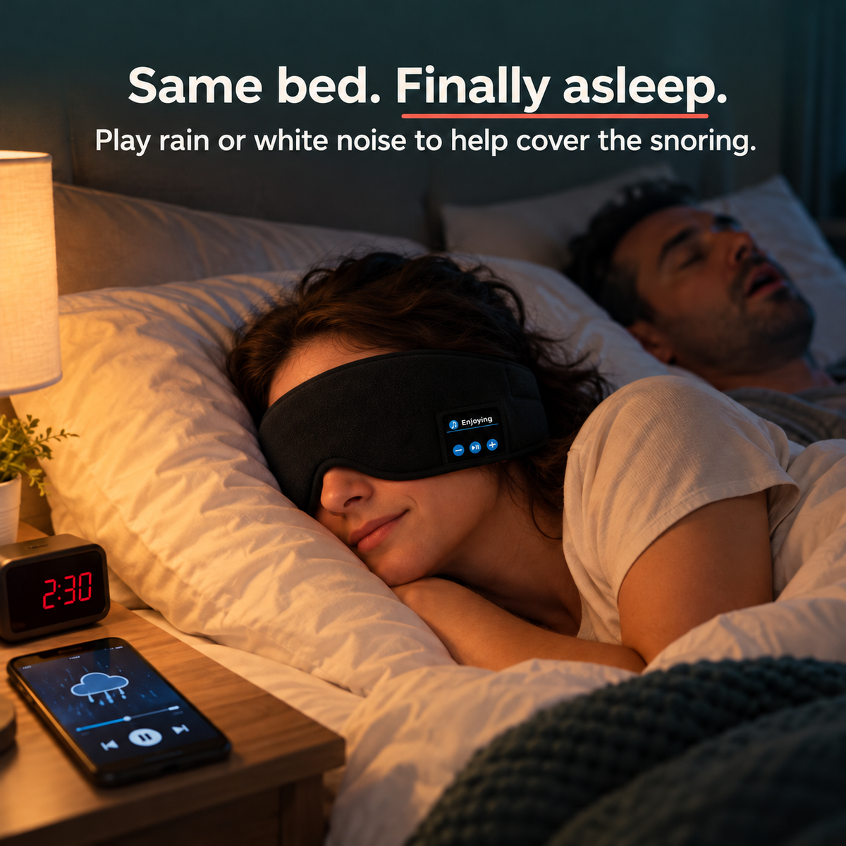 Woman asleep in the DreamShade mask next to her snoring partner, rain sounds playing on her phone